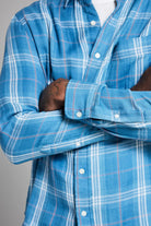 Close-up of a person wearing a blue plaid shirt with arms crossed on a gray background