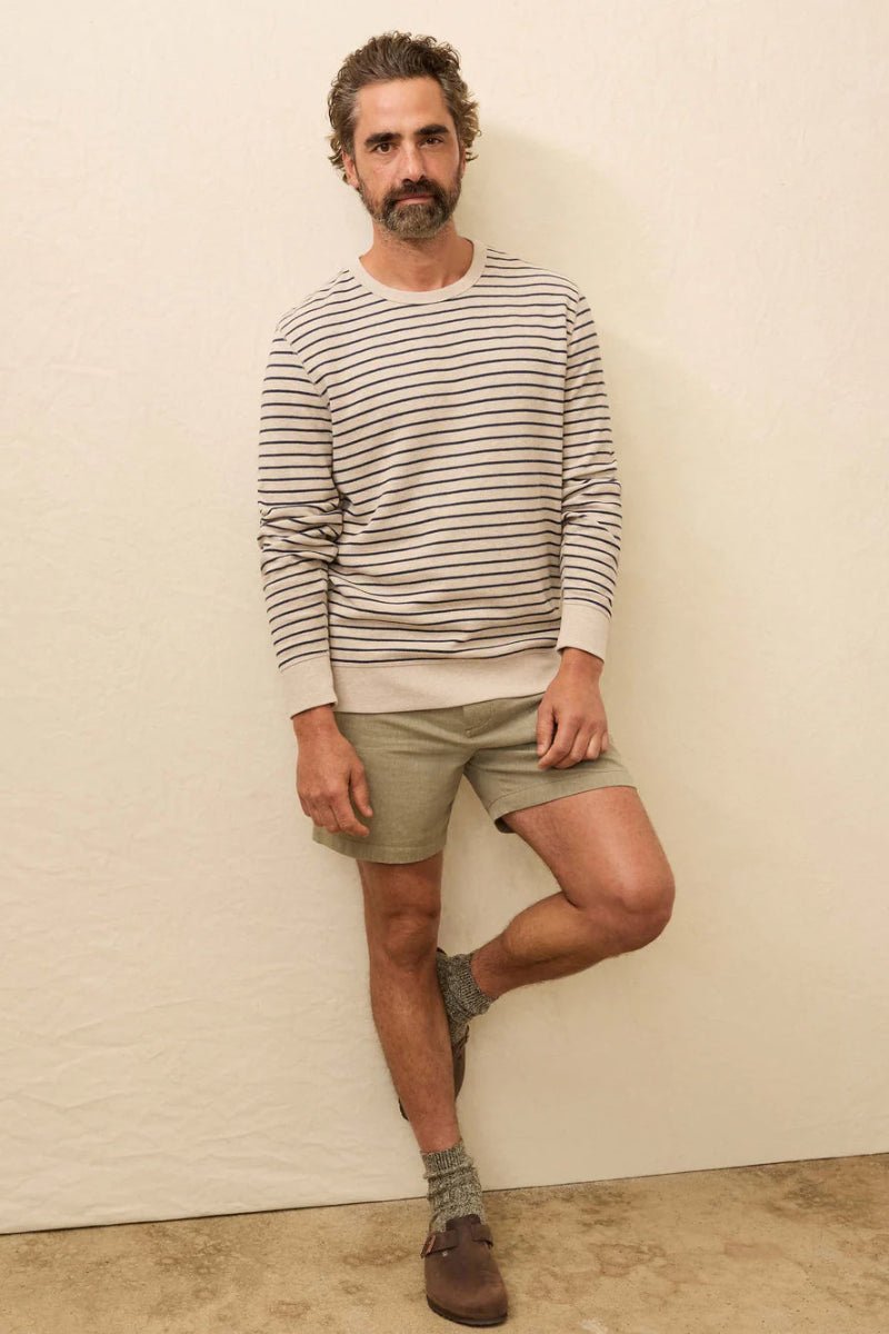 Man wearing a striped sweater and shorts against a plain wall.