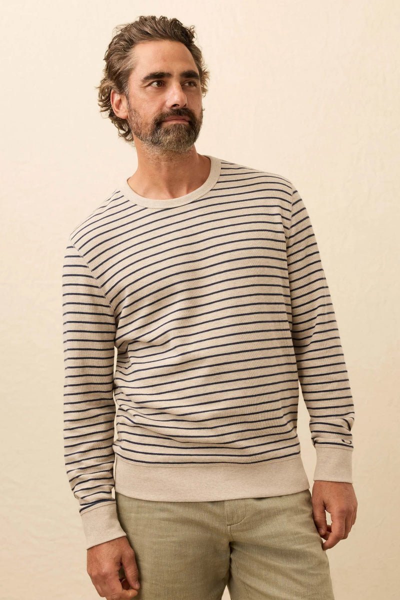 Man wearing a striped sweater and beige pants against a beige background