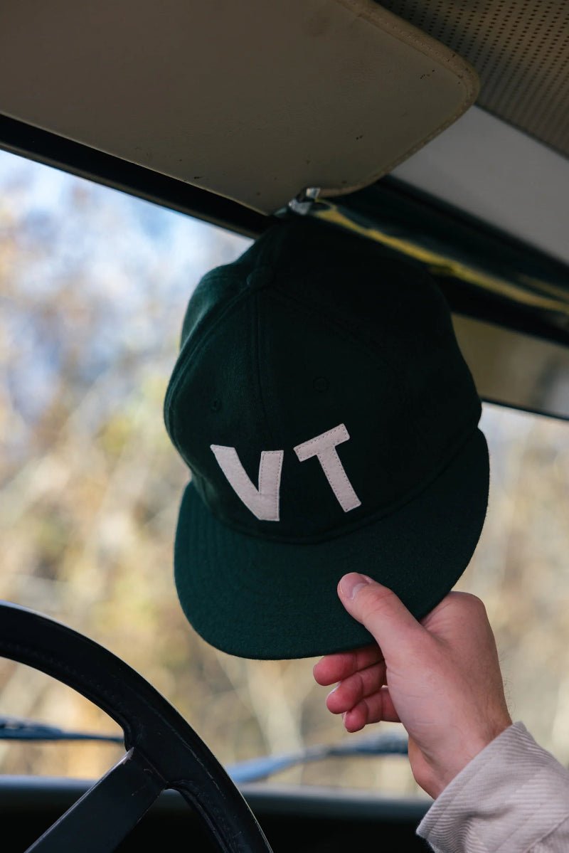 Hand holding a green cap with 'VT' on it inside a vehicle.
