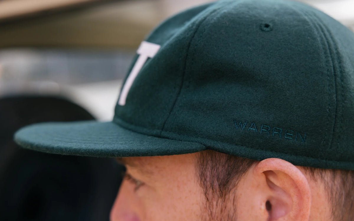 Close-up of a person wearing a green cap with a logo, blurred background