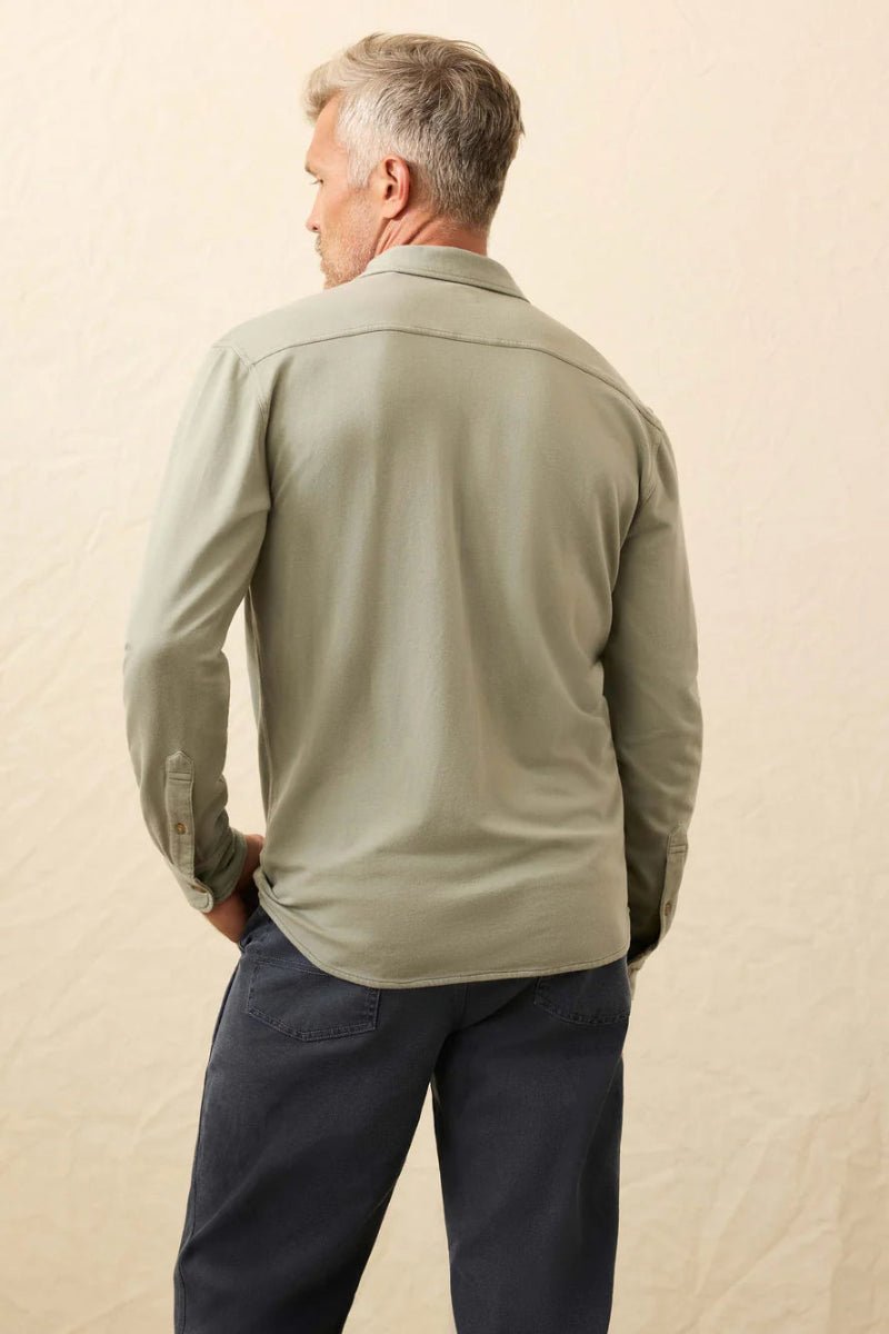 Man wearing a light green shirt and dark pants against a beige background