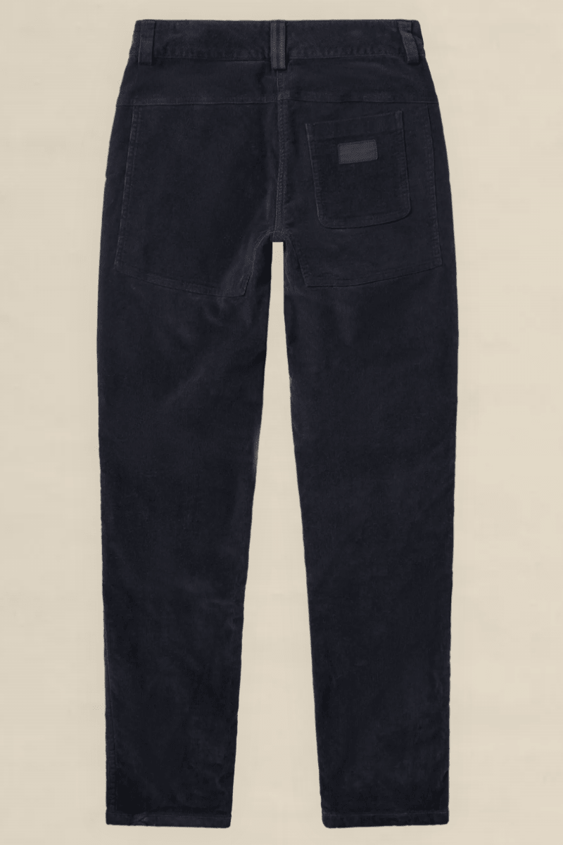 Rear view of dark navy corduroy trousers on a light beige background.