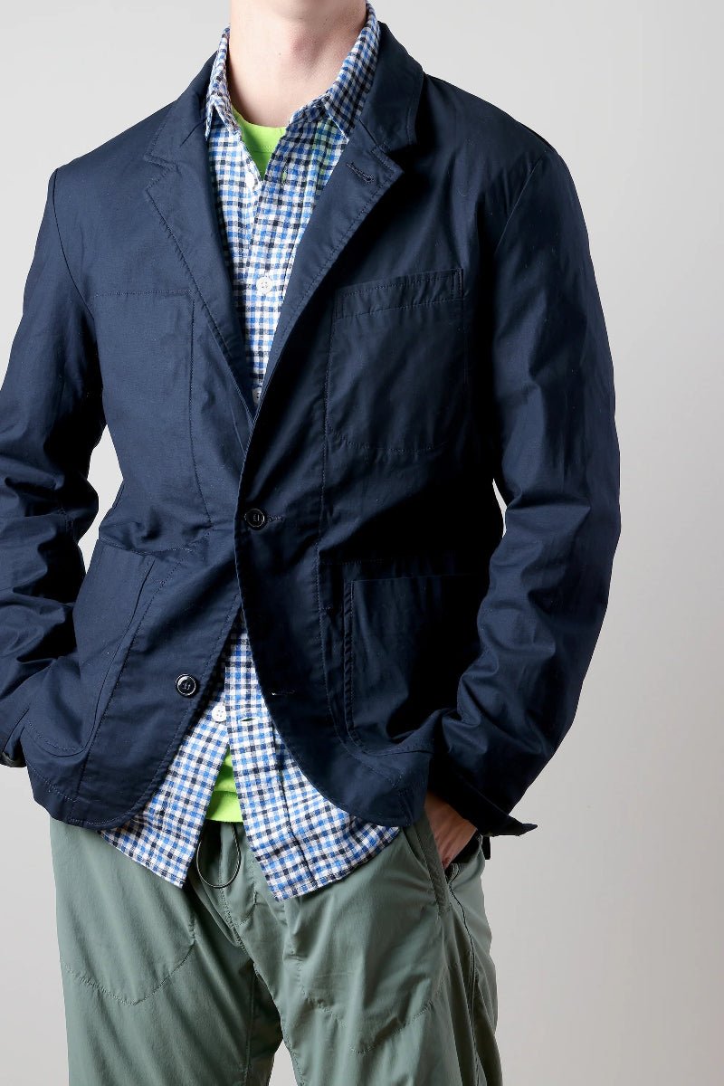 Person wearing a navy jacket over a checkered shirt with a plain background