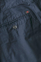 Close-up of dark blue pants with a button and brand logo on the pocket.