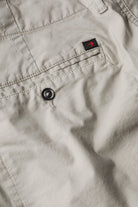 Close-up of beige pants with a button and brand logo on the pocket.