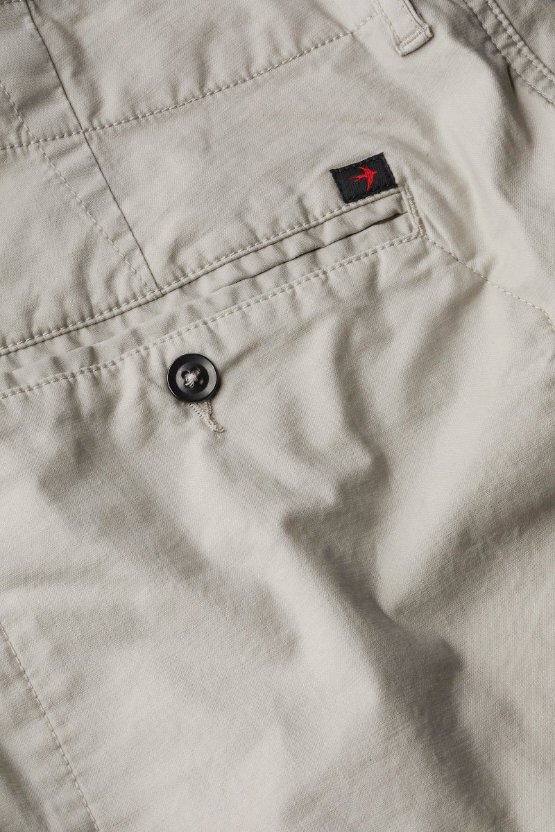 Close-up of beige pants with a button and brand logo on the pocket.