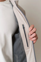 Close-up of a person wearing a light-colored jacket with a zipper pocket.