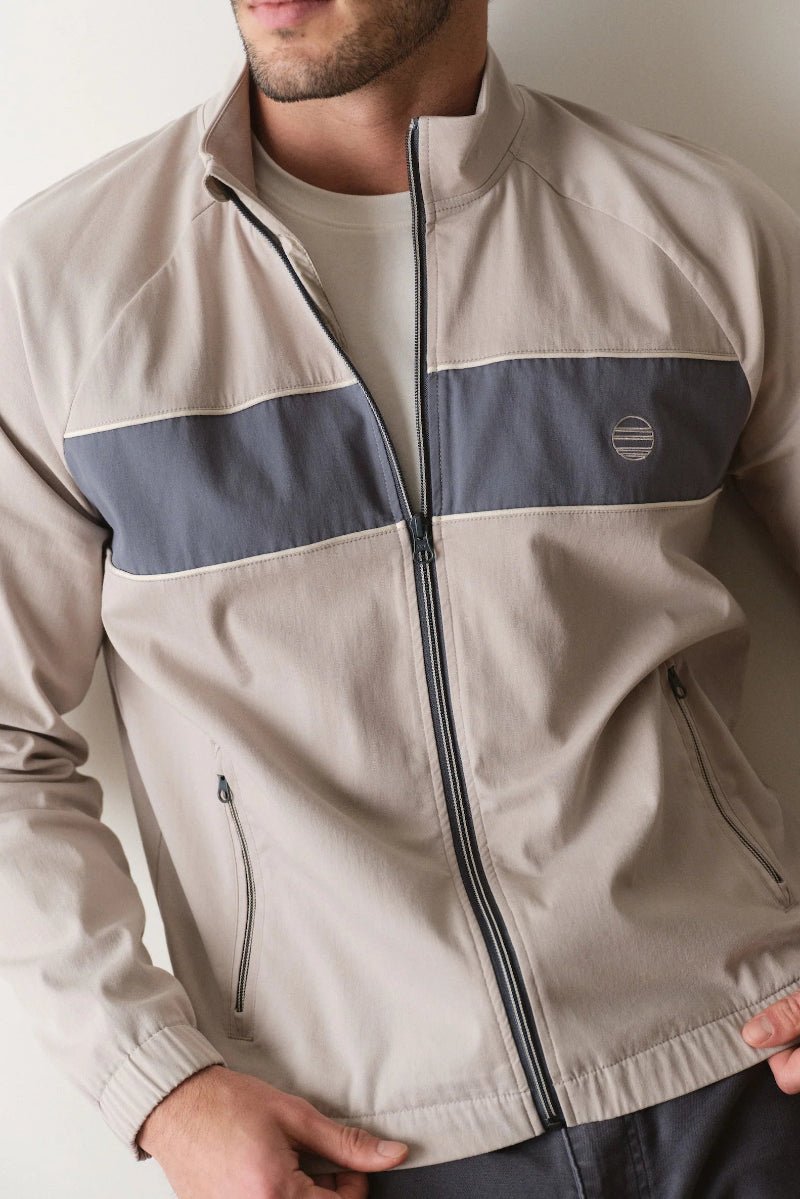 Man wearing a beige and navy jacket with a logo on a plain background