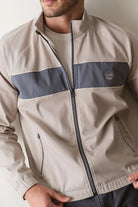 Man wearing a beige and navy jacket with a logo on a plain background