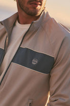 Man wearing a beige jacket with a logo on a blurred background