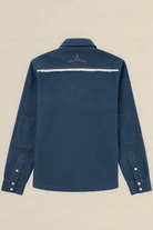 A navy blue long-sleeve shirt jacket shown from the back, featuring a horizontal white stripe across the upper back with a small brown embroidered logo above it, set against a solid beige background.