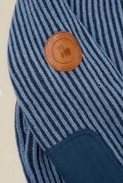 Close-up of a blue and navy striped knit garment with a round brown leather patch reading 'SUPPORT OF ALL VOLS' and a dark navy patch pocket.
