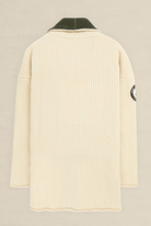 A cream-colored ribbed knit sweater shown from the back, featuring a dark olive green collar and a circular patch on the left sleeve, set against a light beige background.