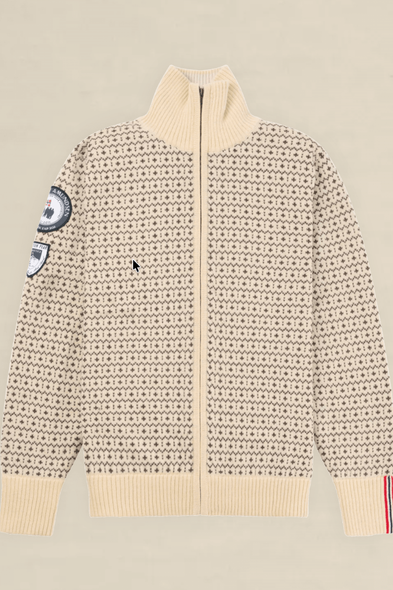 A cream-colored knit zip-up sweater with a dense black geometric pattern, featuring a mock neck, ribbed cuffs and hem, and decorative patches on the sleeves, displayed flat against a light beige background.