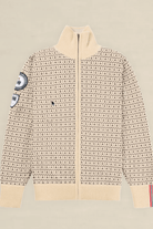 A cream-colored knit zip-up sweater with a dense black geometric pattern, featuring a mock neck, ribbed cuffs and hem, and decorative patches on the sleeves, displayed flat against a light beige background.
