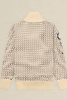 A cream-colored knit sweater with a dense black geometric pattern, featuring a ribbed mock neck, cuffs, and hem, with a circular patch on the right sleeve, shown against a solid light beige background.