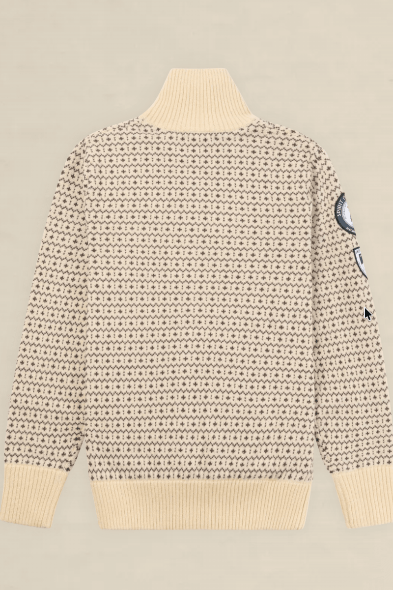 A cream-colored knit sweater with a dense black geometric pattern, featuring a ribbed mock neck, cuffs, and hem, with a circular patch on the right sleeve, shown against a solid light beige background.