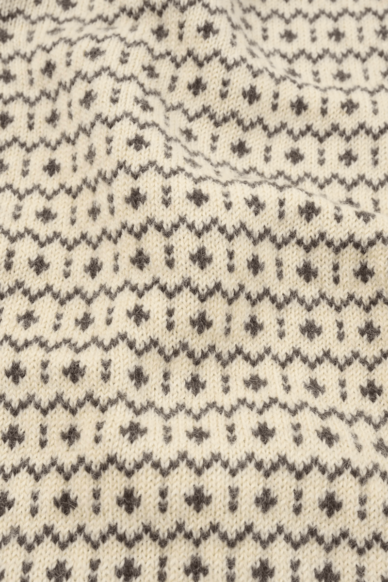 Close-up of a cream-colored knit fabric with a dark gray Fair Isle pattern of small geometric motifs.