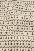 Close-up of a cream-colored knit fabric with a dark gray Fair Isle pattern of small geometric motifs.