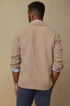 Man wearing a beige blazer over a white shirt with rolled-up sleeves on a beige background