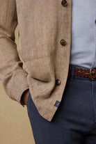 Close-up of a person wearing a beige blazer, light blue shirt, and navy pants with a brown belt.