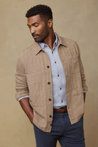 Man wearing a beige jacket over a light blue shirt with a brown background