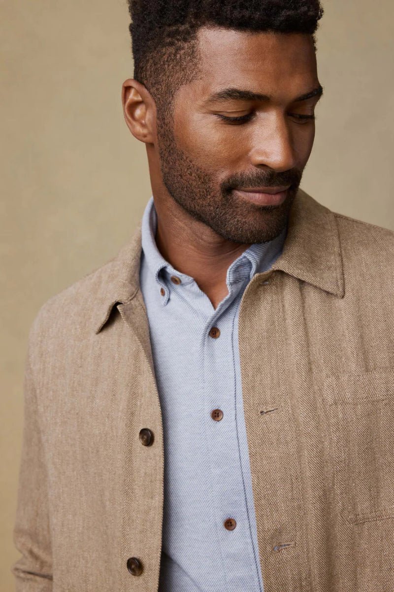 Man wearing a beige jacket over a light blue shirt against a beige background