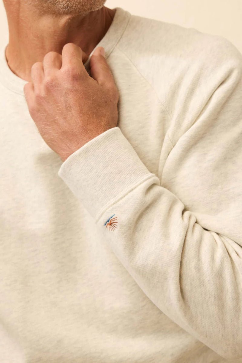 Close-up of a person wearing a beige sweater with a brand logo on the sleeve.