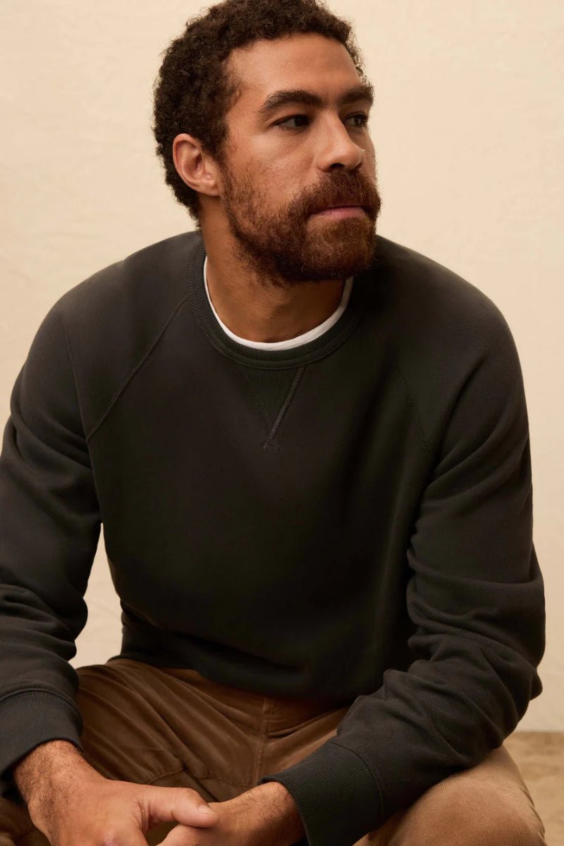 Man wearing a dark sweater and brown pants sitting against a beige background