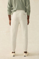 Person wearing light gray sweatpants and a green long-sleeve shirt on a beige background