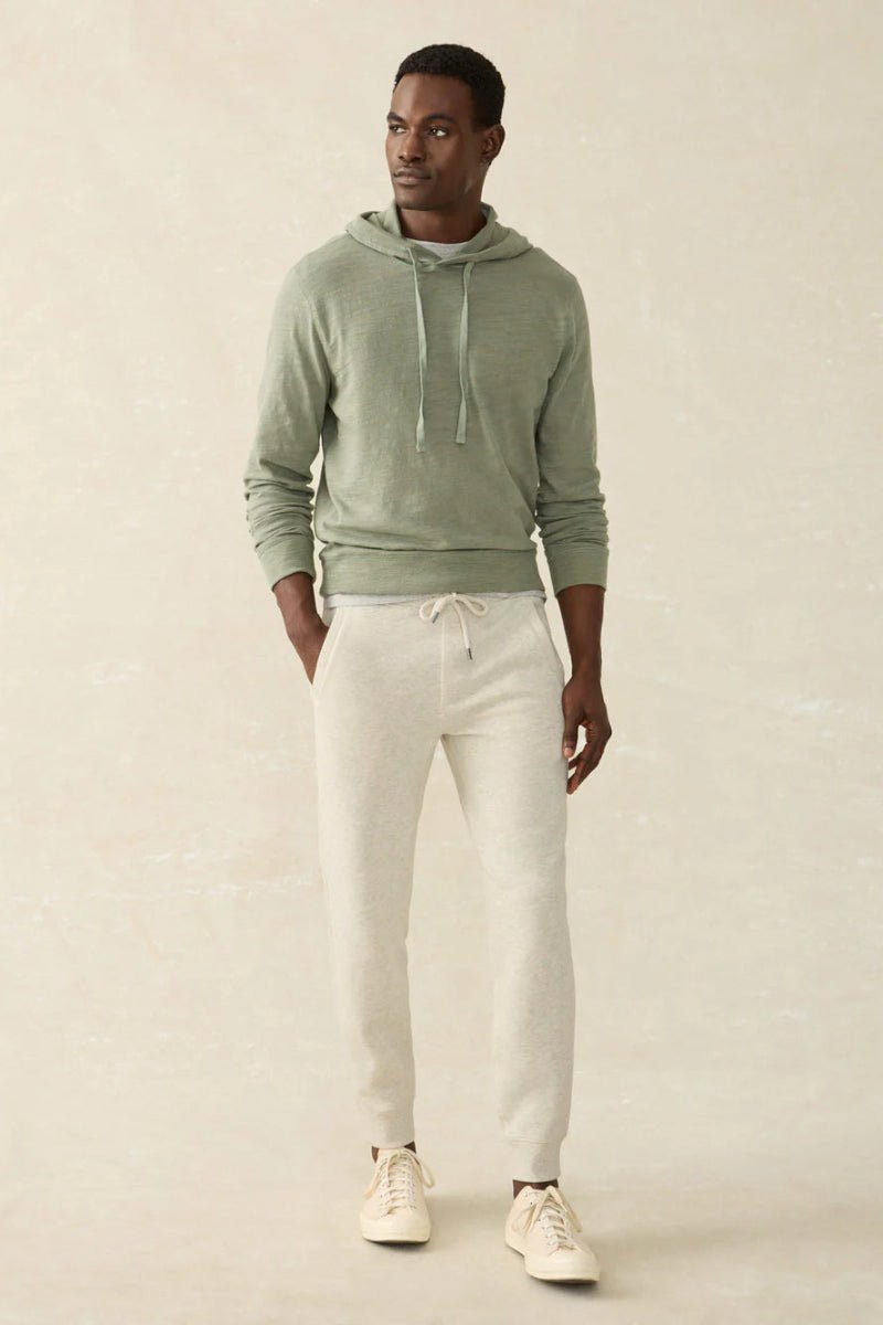 Man wearing a green hoodie and white pants on a beige background
