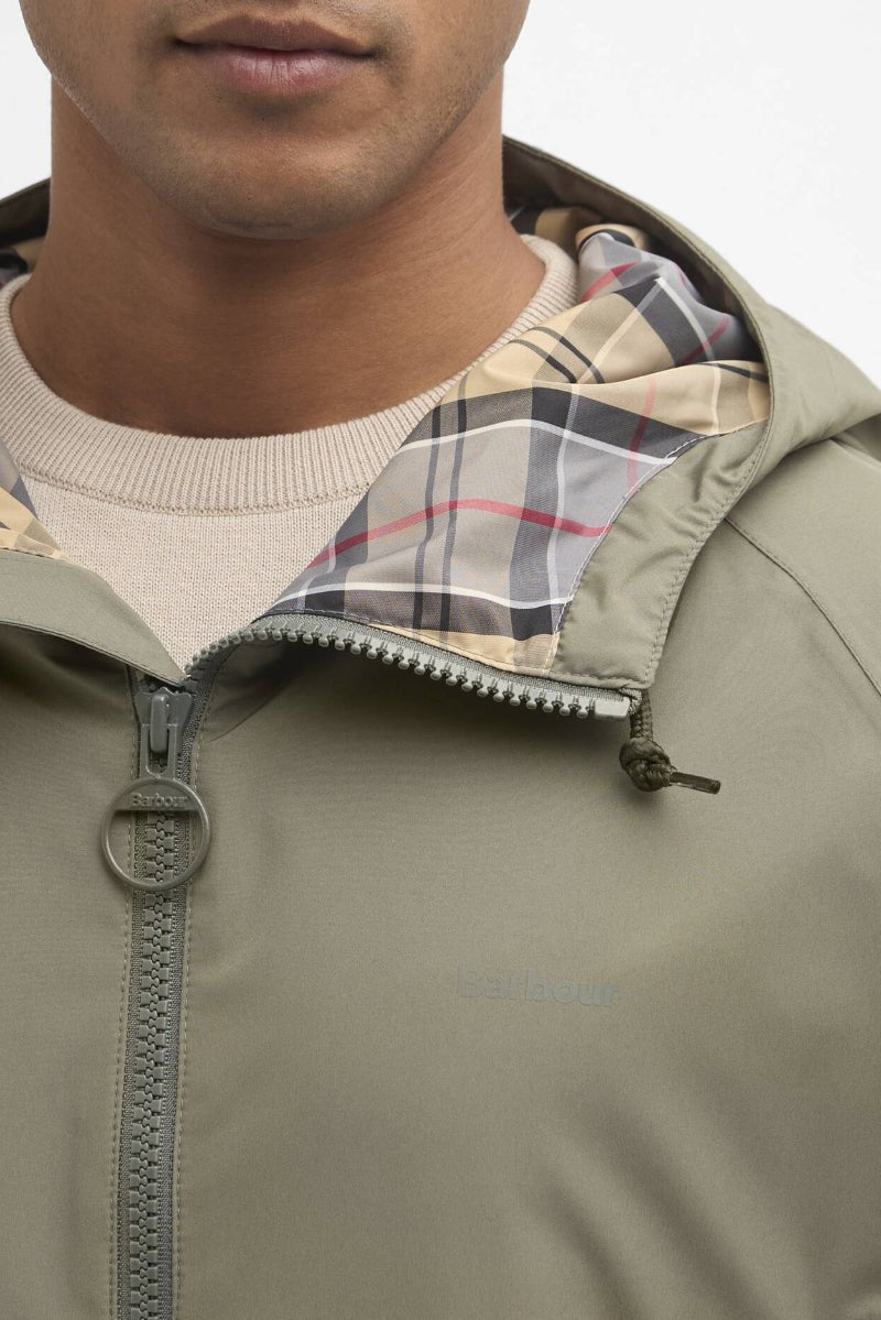Close-up of a person wearing a beige jacket with plaid lining on a neutral background