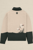 Back view of a knit sweater in beige and dark green, featuring a small embroidered floral motif near the lower right side and a circular black logo patch at the neck.