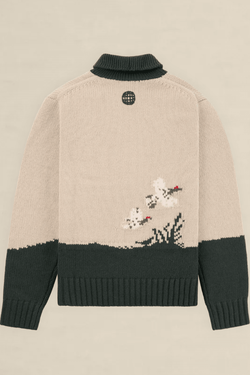 Back view of a knit sweater in beige and dark green, featuring a small embroidered floral motif near the lower right side and a circular black logo patch at the neck.