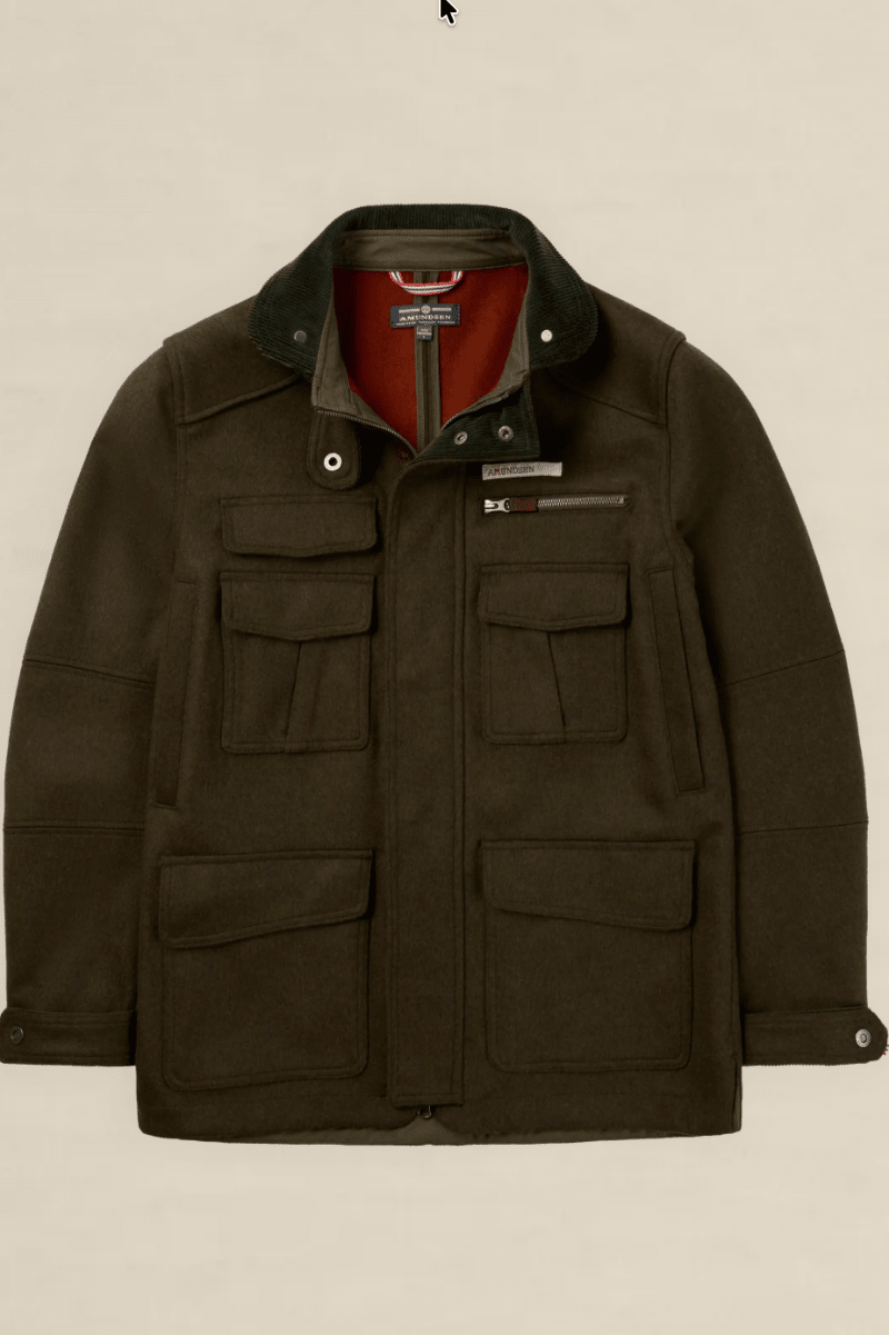 A dark olive green waxed cotton jacket with a corduroy collar, multiple front flap pockets, and a red inner lining, shown against a solid light beige background.