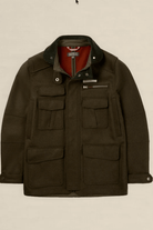 A dark olive green waxed cotton jacket with a corduroy collar, multiple front flap pockets, and a red inner lining, shown against a solid light beige background.