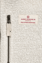 Close-up of a textured off-white fleece jacket featuring a black metal zipper with a matching beige fabric pull tab and a sewn-on brand label reading 'AMUNDSEN SPORTS FIELD TESTING ADVENTURES'.