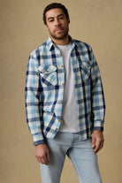 Man wearing a blue and white plaid shirt over a white t-shirt on a beige background