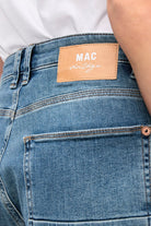 Close-up of blue jeans with a visible MAC label on a white background