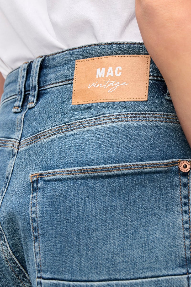 Close-up of blue jeans with a visible MAC label on a white background