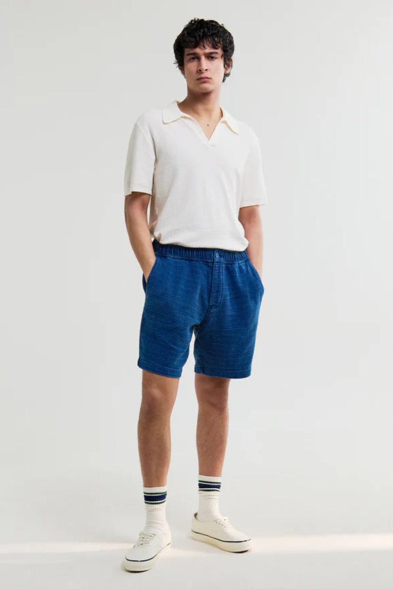 Person wearing a white polo shirt and blue shorts on a white background
