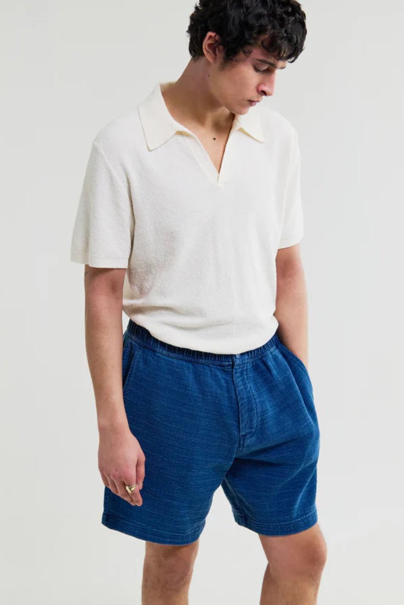 Person wearing a white polo shirt and blue shorts on a plain background