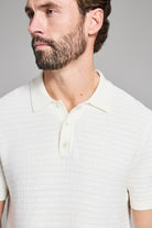 Man wearing a white polo shirt against a gray background