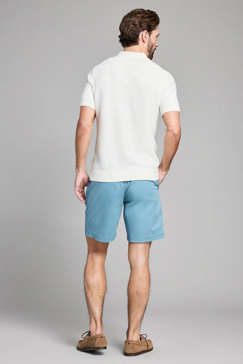 Man wearing a white polo shirt and light blue shorts on a gray background