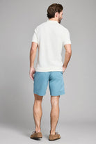 Man wearing a white polo shirt and light blue shorts on a gray background