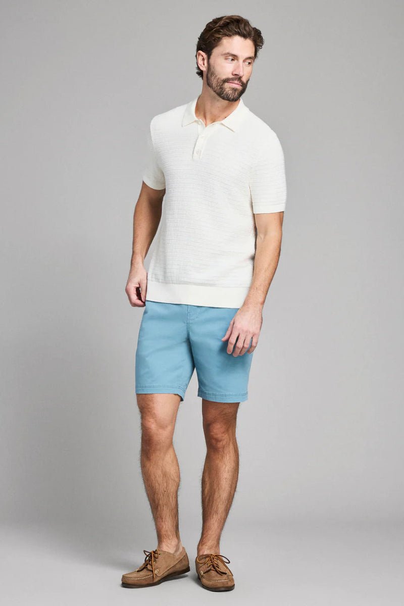 Man wearing a white polo shirt and light blue shorts on a gray background