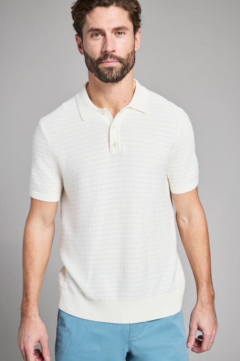 Man wearing a white textured polo shirt and blue pants on a gray background