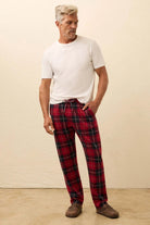 Man wearing a white t-shirt and red plaid pants against a beige background