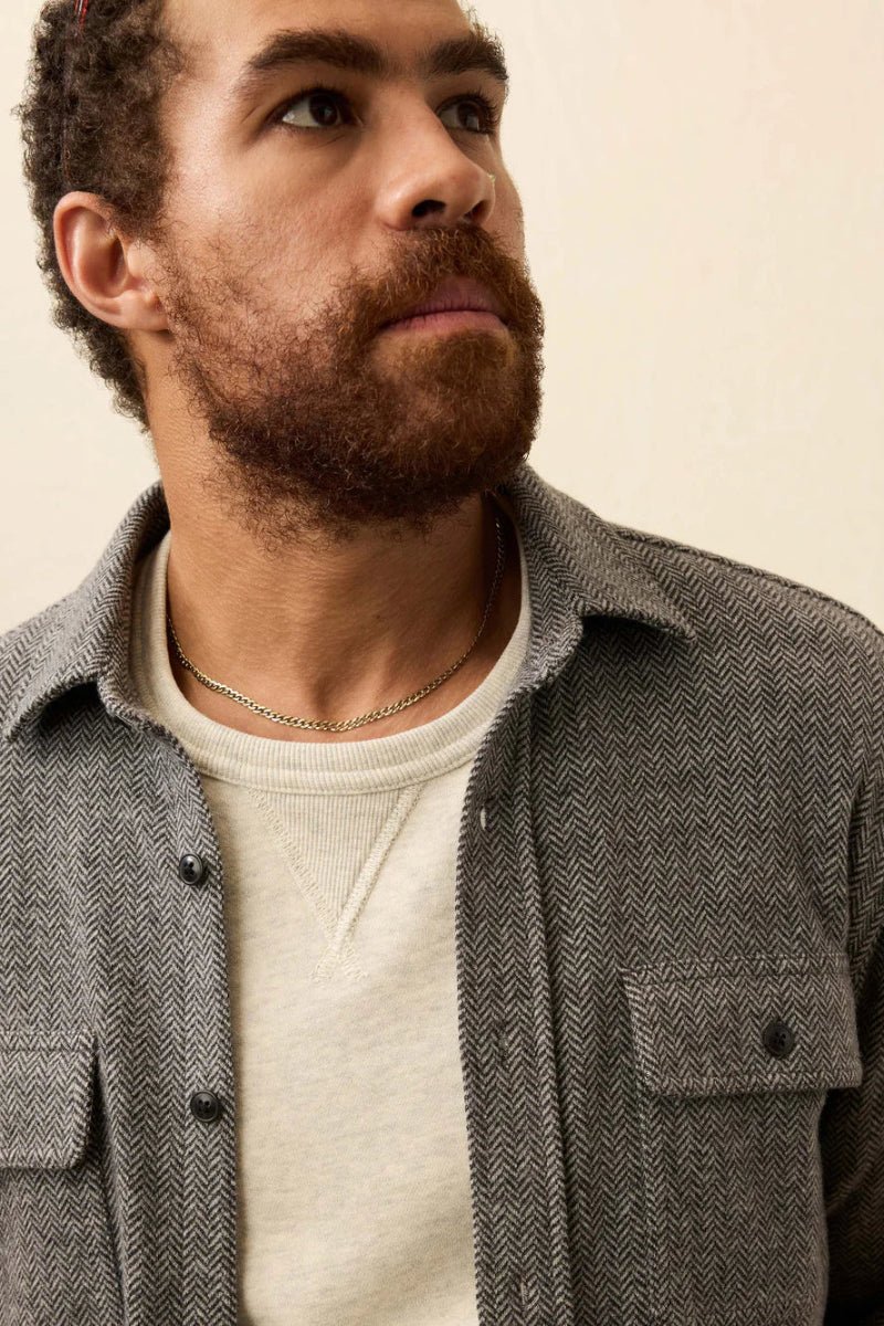 Man wearing a gray textured shirt over a white sweater against a beige background